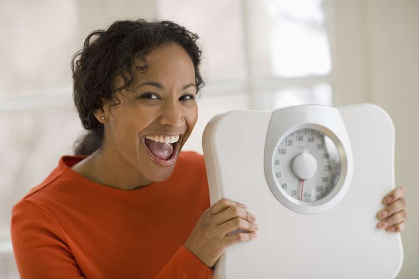 Happy black woman holding scale